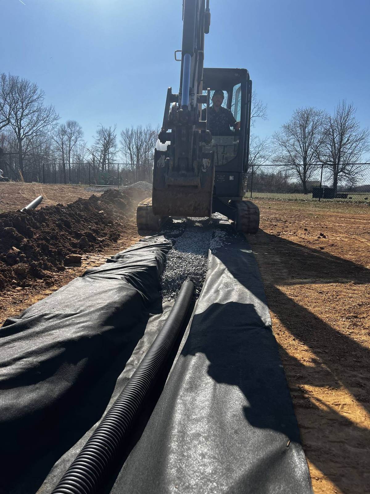 Excavator installing drainage pipe in an open trench